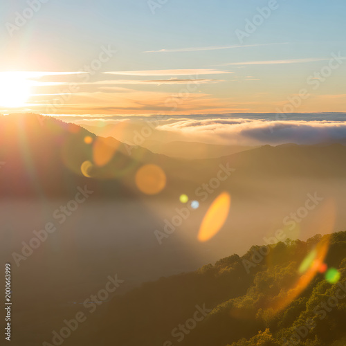 Sunrise over mountains with fog and lens flares in the foreground creating a serene and peaceful atmosphere in nature