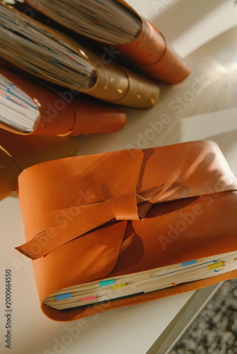 Closeup of a leather notebook with brown cover, pages peeking, tabs and bookmarks visible, lying on a desk with writing tools, highlighting a traditional writing setup