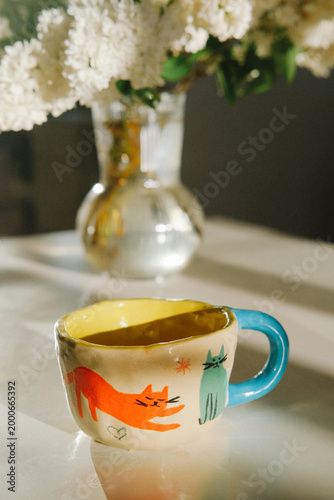 Mug, fox, ceramic, colorful, table, flowers, vase, handle, orange, blue with warm light and soft shadows, stilllife depicting beverage and decorative ceramics