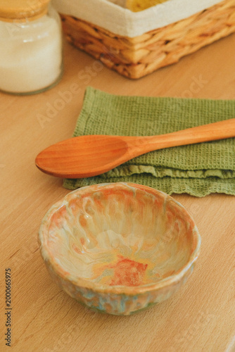 Ceramic pottery bowl with a wooden spoon on a green napkin, set on a wooden table, highlighting handmade craft, rustic decor, and simple kitchenware for everyday dining.