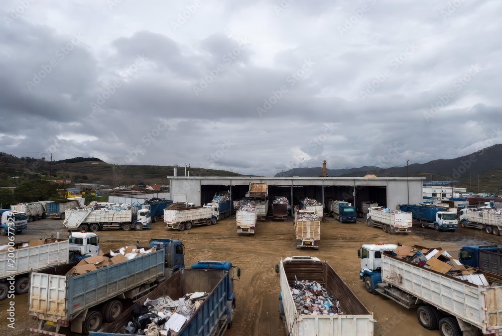Fototapeta premium Recycling center with trucks full of waste and cardboard under a cloudy sky