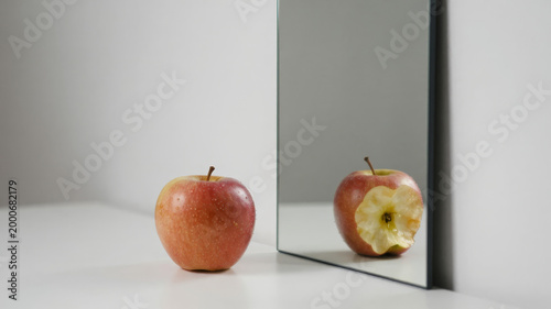 Fresh red apple with mirrored reflection showing whole and bitten fruit in clean white studio for healthy nutrition and food concept display