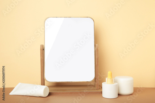 Set of various skincare products standing on beige background with stylish mirror. Top view