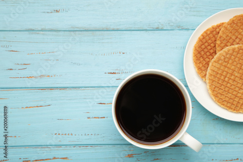 Traditional local authentic Dutch Netherlands sweet fresh homemade tasty stack brown golden waffle melt salted caramel with hot warm coffee. Stroopwafel on blue background