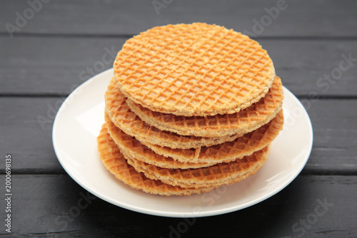 Stack of Dutch stroop wafel cookies or caramel waffles on plate on black background. Space for text