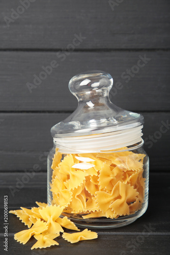 Raw farfalle pasta on glass jar on black background. Vertical photo