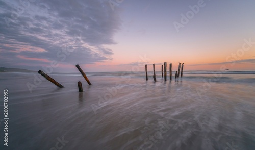 Old broken bridge, posts in the water on the beach at dusk, St. Clair, Dunedin, Southland, New Zealand