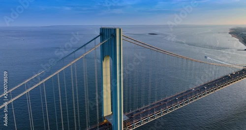 Rising over the riverscape near the support of modern Verrazzano-Narrows Bridge. Cars move quickly by the bridge at sunset.