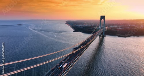 Beautiful scenery of the Verrazzano-Narrows Bridge with lively traffic. Stunning orange sky over the waterscape and cityscape in the backdrop. Aerial view.