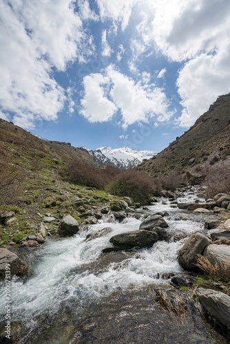 Mountain stream Rio Valdeinfierno, hiking trail near Junta de los Rios, behind Sierra Nevada with summits Mulhacén and La Alcazaba, snow-covered mountains near Granada, Andalusia, Spain