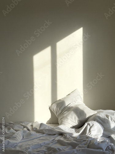 Golden morning sunlight casting window shadows on rumpled white bed sheets and soft pillows in minimalist cozy bedroom interior scene