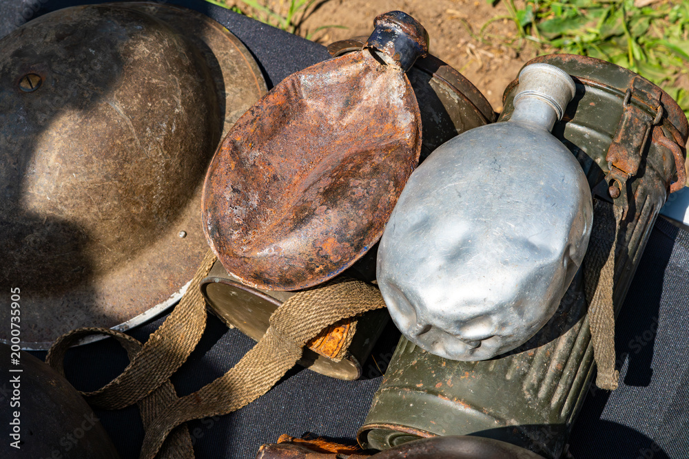 Naklejka premium Collection of vintage military artifacts on a dark background: steel helmet, rusty canteen, dented aluminum flask, and a gas mask canister. Close-up view of historical war equipment and textures.