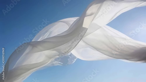 Billowing white fabric ruffling in wind, forming sunlit twisting ribbon shapes against blue sky