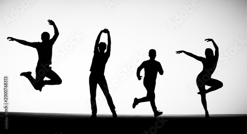 Silhouettes of people dancing and jumping against a bright background.