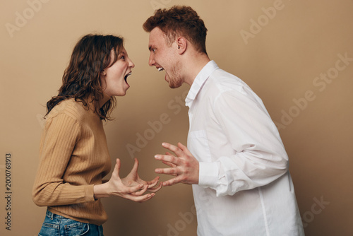 Фотография Angry young man and woman shouting at each other in casual clothes on beige background
