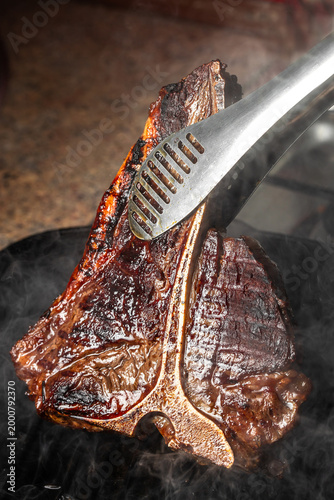 Obraz na płótnie Grilled t-bone steak being flipped with tongs on hot pan, juicy seared crust