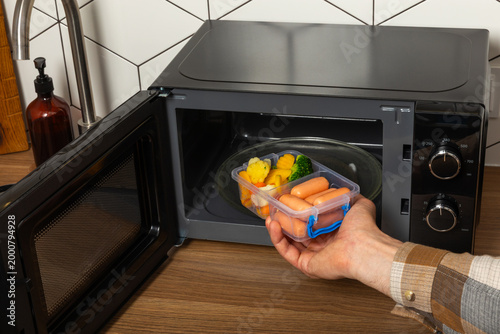 Tableau sur toile Man putting Lunch Box with lunch into microwave indoors