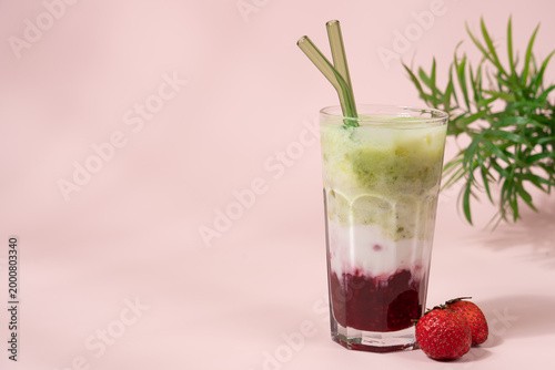 Strawberry matcha latte in clear glass on pastel light pink background with copy space, layered iced drink, minimal aesthetic