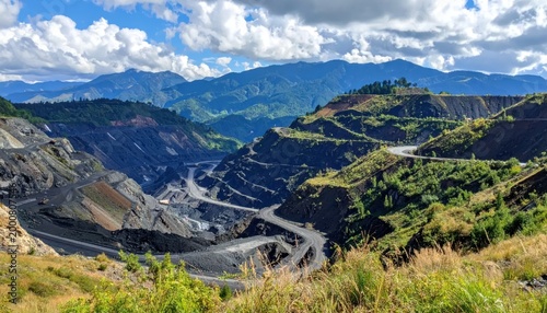 Expansive Open Pit Mine Carved into Lush Green Mountains Under a Cloudy Sky.
