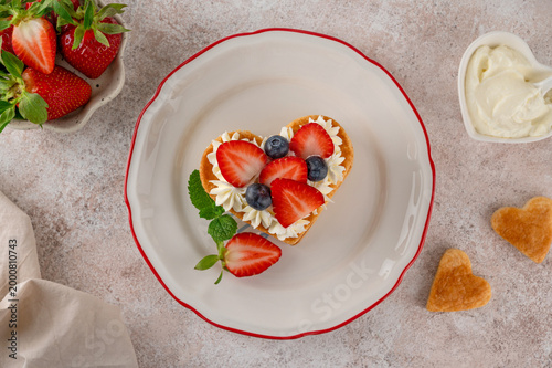 Valentines day dessert. Heart shaped cake millefeuille with vanilla cream and fresh berries on a plate on a light concrete background. Romantic food concept. Top view.