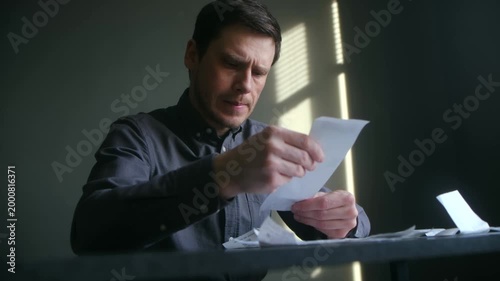 Serious man sitting at table checking his household expenses and receipts, looking worried about his financial situation, calculating costs and payments during an economic crisis. 