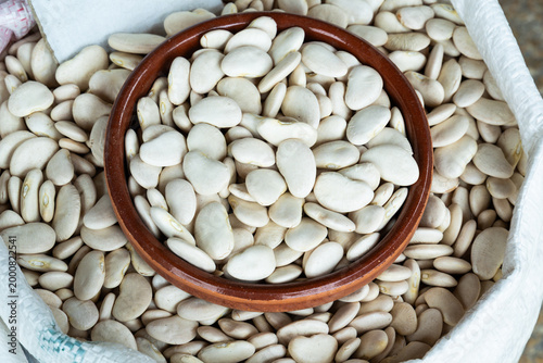 Large dry white lima beans filling a ceramic bowl on a rustic market display. High-quality top view highlighting natural texture for healthy eating, vegan diet, and grocery themes