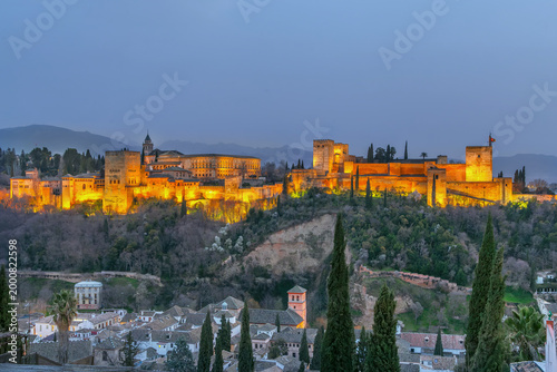 Illuminated Alhambra palace complex in Granada Spain at evening. Panoramic view from San Nicolas viewpoint under dusk sky