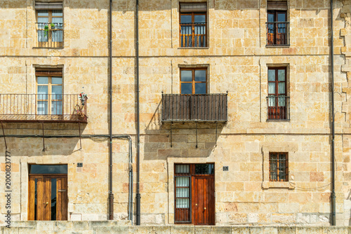 Facade of a historic stone building in Salamanca, Spain with traditional wooden doors, windows, and iron balconies. A beautiful example of European heritage and classical architecture