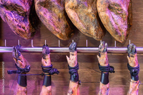 Traditional Spanish Jamon Iberico ham legs hanging in a deli shop. High-quality cured meat with black hooves (Pata Negra) displayed on a wooden wall in a gourmet restaurant