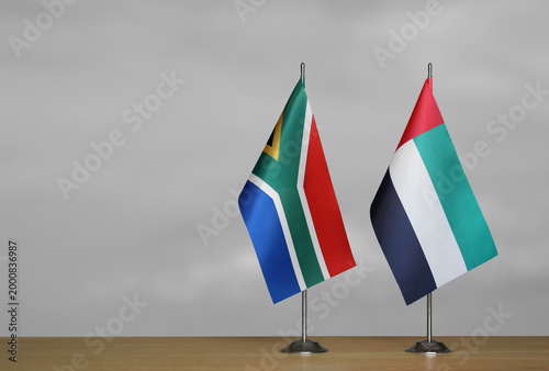 Two table flags of the South Africa and Emirates on a blurred gray background