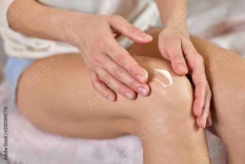 Woman's hands applying white moisturizing cream to her knee, providing skincare, muscle relaxation, and joint pain relief