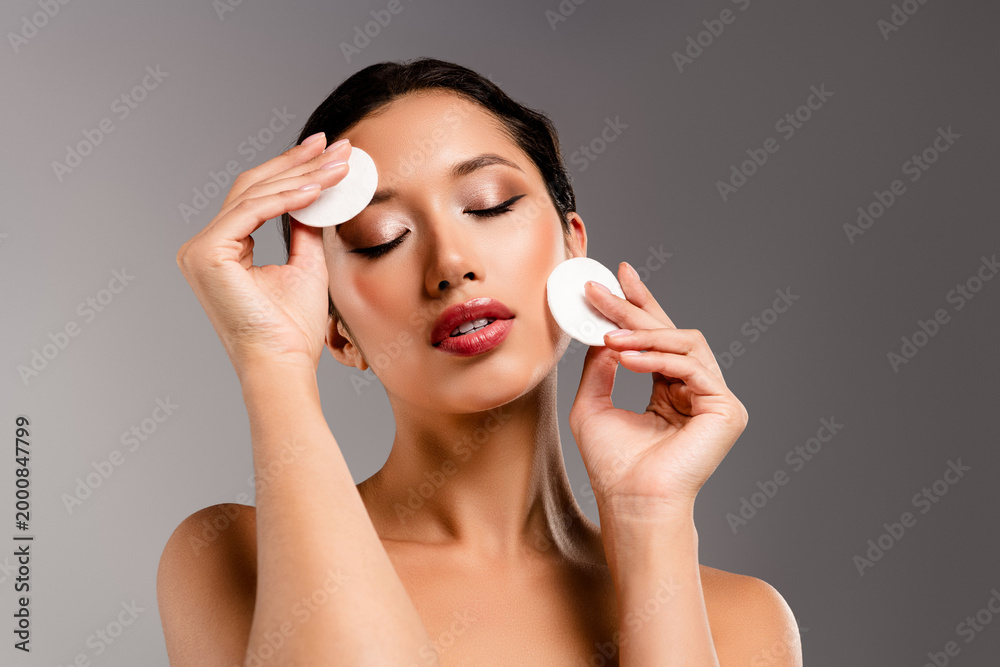 Fototapeta premium Beauty focused portrait of a young asian woman applying cotton pads to her face for skincare and spa inspired treatment