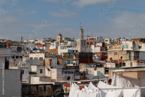 Tanger urban panoramic view showing medina rooftops, minaret, clock tower, and satellite dishes under blue sky