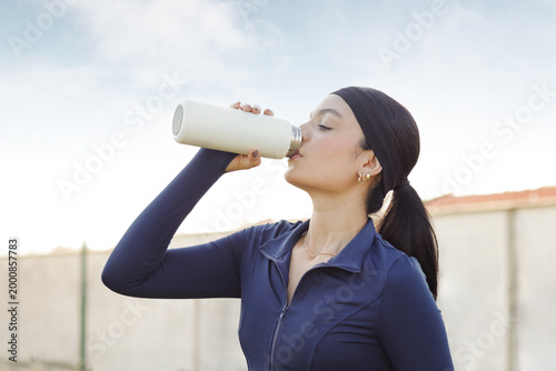 Woman hydrating with a reusable bottle after exercise, refreshing outdoor fitness activity, healthy and active lifestyle