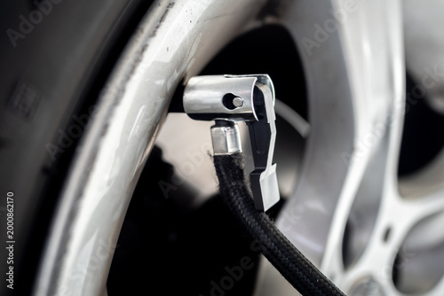Detailed close-up of an air pump nozzle connected to a car tire valve on an alloy wheel - concept of vehicle maintenance, tire inflation and safety check