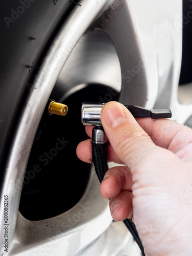 Close-up of a hand connecting an air pump to a car tire valve on an alloy wheel - concept of vehicle maintenance, tire inflation and safety check