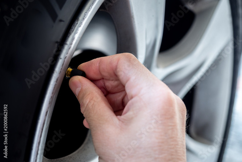 Close-up of a hand screwing a cap onto a car tire valve on an alloy wheel - concept of vehicle maintenance, tire inflation and safety check