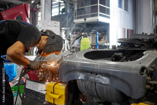 .A dedicated service center employee, wearing a protective mask, skillfully welds to repair a truck. The scene captures the precision and attention to detail involved in vehicle maintenance.