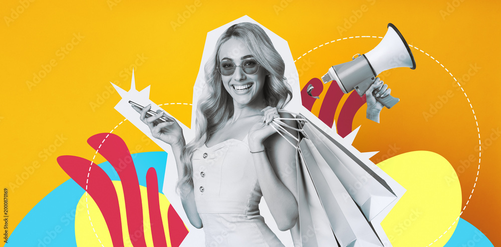 Fototapeta premium A young woman with long blonde hair smiles while holding colorful shopping bags and a smartphone. She stands in front of a bright yellow background.