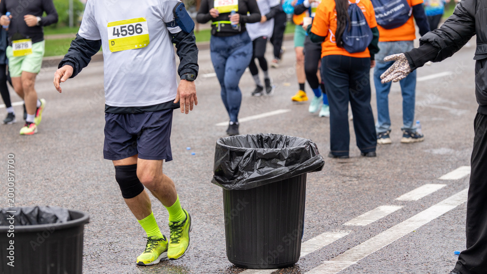 Fototapeta premium Runners passing by garbage cans at a city running event