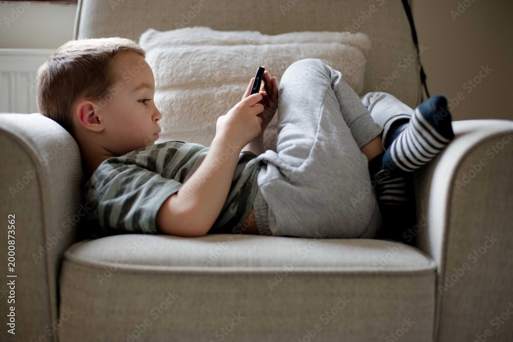 Obraz premium Child young boy using smartphone playing game relaxed at home