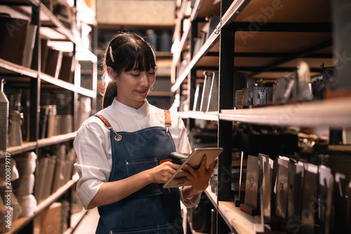 Young woman using tablet in warehouse aisle, inventory check in storage room with shelf and package
