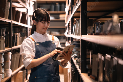 Fotografía Young woman in apron using tablet in storage room