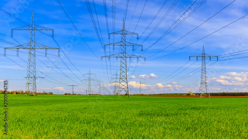 Photography Power lines stretch across a green field under a blue sky with clouds in the bac