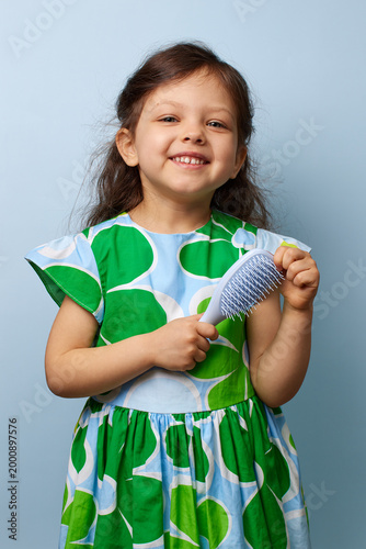 adorable toddler girl smiling happily while holding a hairbrush on blue background, emphasizing childhood care