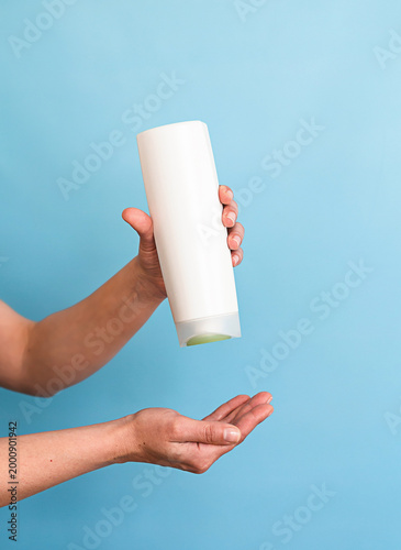 a woman's hands hold a white shampoo bottle on a blue background