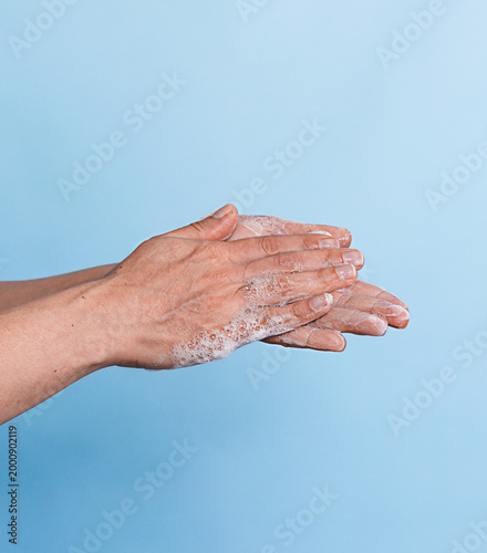 soapy hands of a middle-aged woman on a blue background
