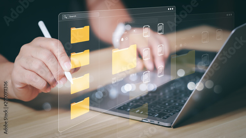 Businessman hands using stylus pen with futuristic virtual document management system and floating digital folders on laptop. Cloud storage, paperless office, and online data organization concept.