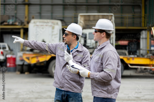 Fotografija Two construction workers in safety gear discuss and point at something on a work site, appearing to coordinate a task
