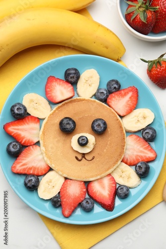 Creative serving for kids. Cute lion made of pancake, banana and berries on table, flat lay